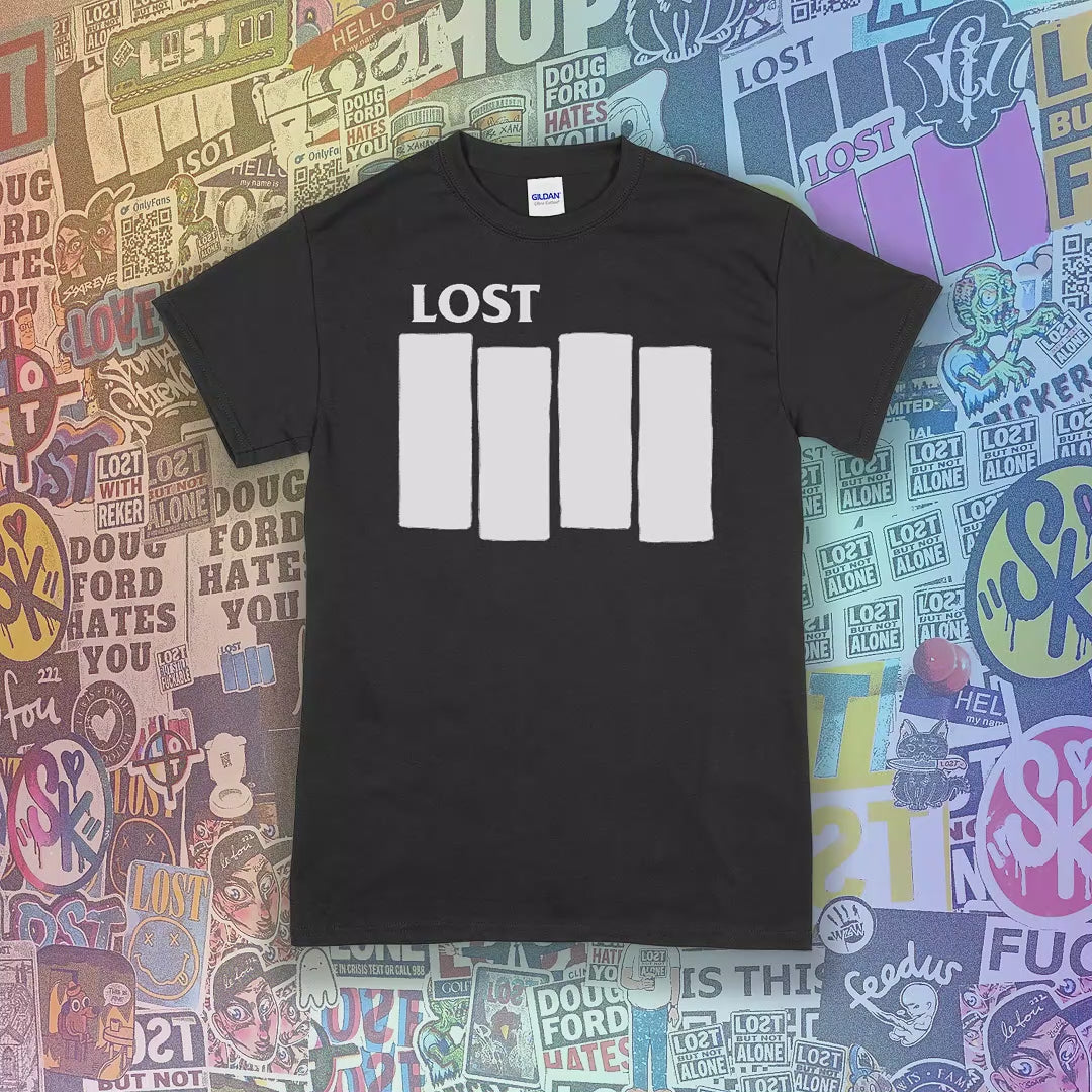 The Lost Flag t-shirt color options are displayed with the iconic bold logo screen printed in white ink on a collection of different colored shirts. A wall of colorful graffiti stickers from artists around the world makes up the background.